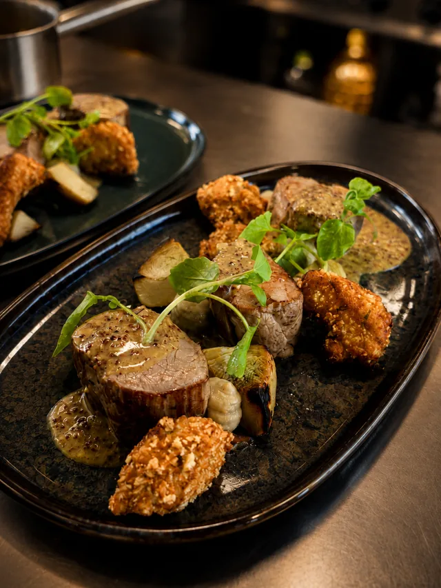 Mignon de veau, jus moutardé, oignons rôtis et croquettes dorées sur assiette émaillée