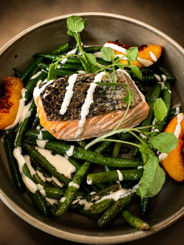 Saumon snacké peau croustillante, haricots verts, pêches et cresson dans un bol en grès